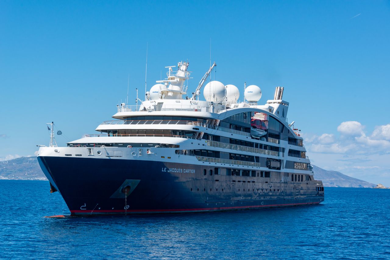 who-we-are A luxury cruise ship sailing on open blue waters under a clear sky.